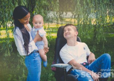 Adam siedzi na wózku, patrzy na swoją żonę Marebel i ich synka Maksymiliana, w tle park