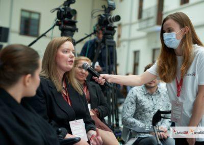 Wolontariuszka trzyma mikrofon obok twarzy Marty Lorczyk, członkini zespołu eksperckiego projektu sekson, która zadaje pytanie. Za nią siedzi dr Alicja Długołęcka. W tle widać kamery.